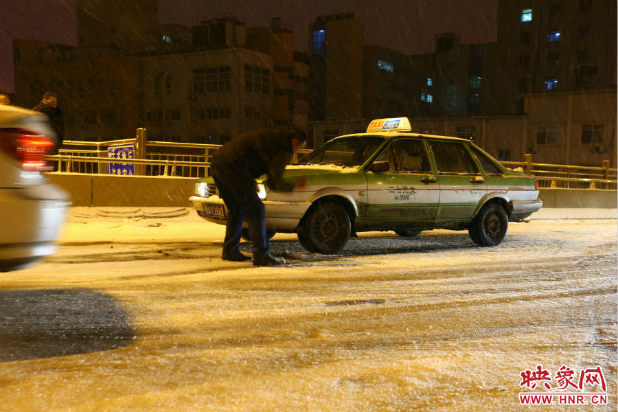 一位出租車司機在車輪前灑上雪，希望能增加輪胎的摩擦力。