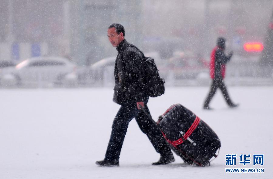 1月19日，旅客冒雪走在沈陽北站站前廣場上。