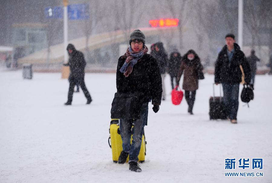 1月19日，旅客冒雪走在沈陽北站站前廣場上。