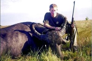 哈里王子手持獵槍，蹲在一頭遭到獵殺的水牛旁邊