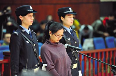 被告人盧梅低著頭，站在朝陽(yáng)法院刑事審判庭的被告席上。